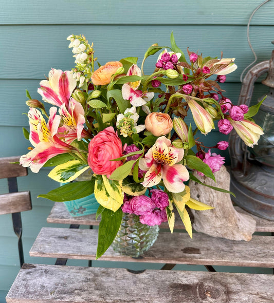 A bright, multi-colored flower arrangement with peach/orange ranunculus, lime-green and yellow foliage and pink/peach/tangerine filler flowers. Arranged in a clean vase for local delivery in West Seattle. 