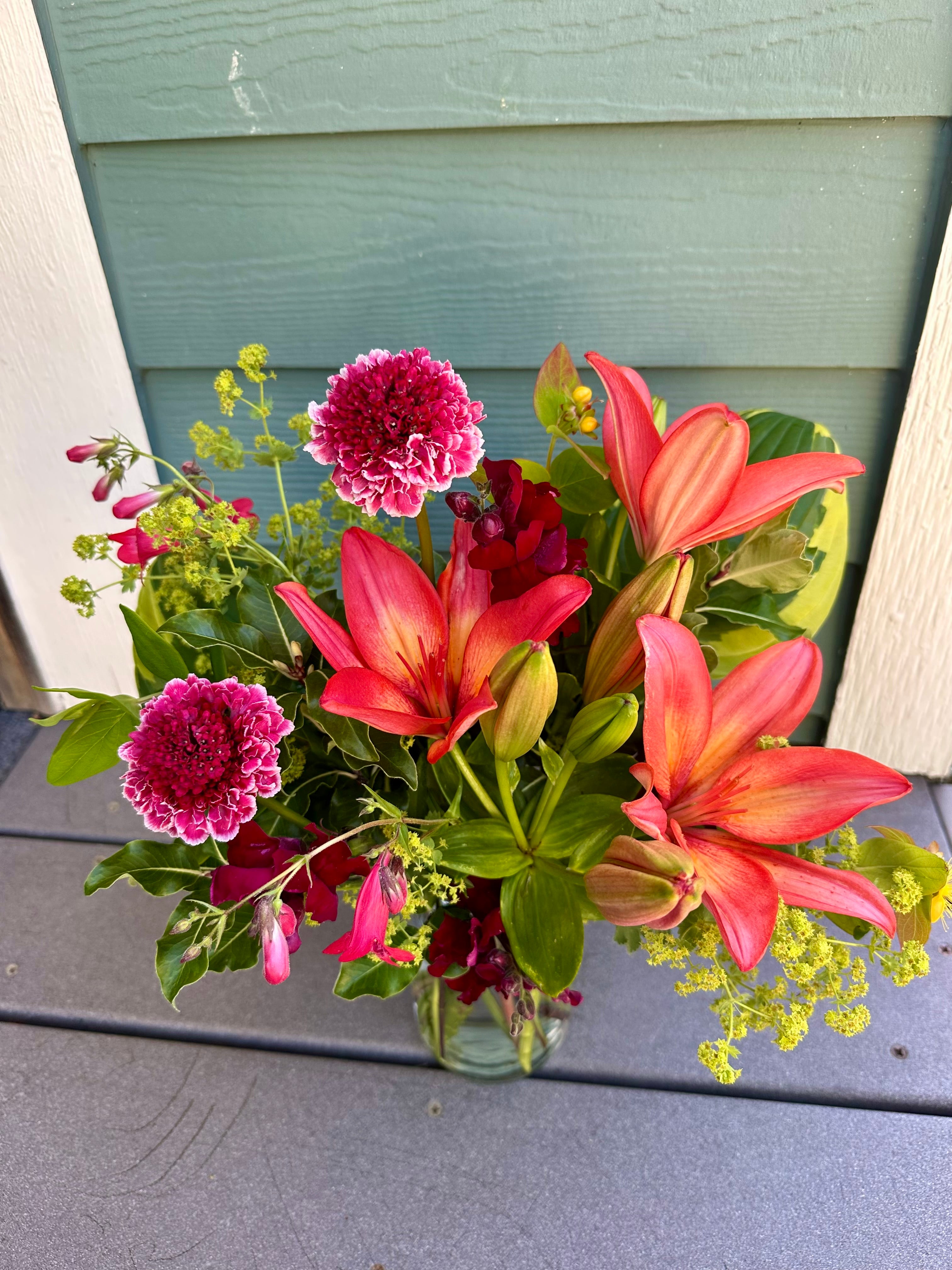 Bouquet of flowers with orange lilies and magenta focal flowers nestled in a wide range of lime-colored greenery