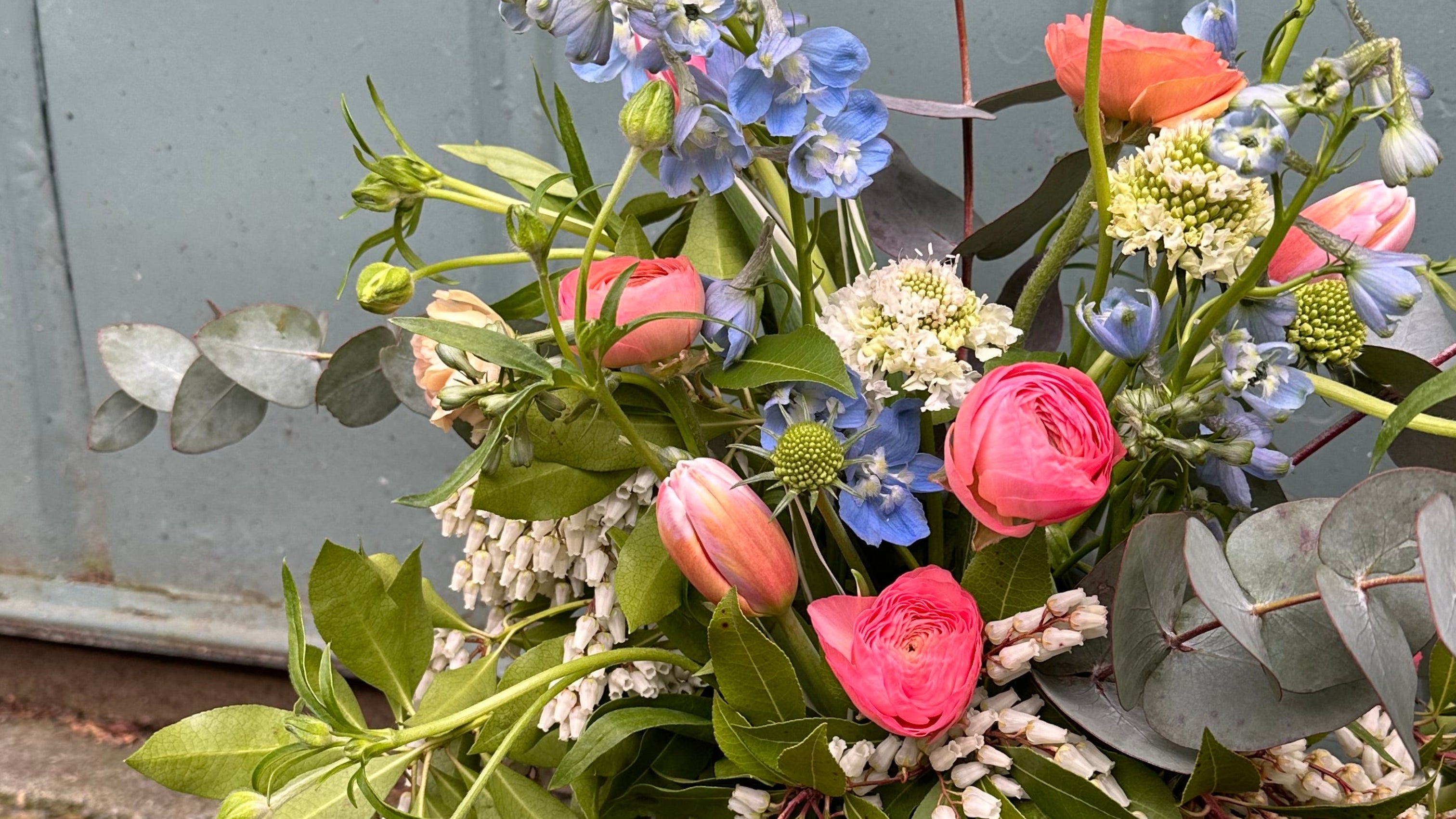 Bouquet of pink and blue spring flowers on a concrete surface with a gray wall in the background