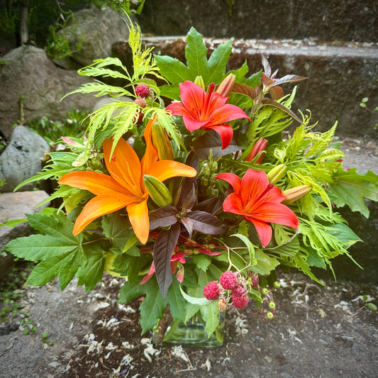Flower Subscription Bouquet of orange and red lilies with green leaves on a stone surface